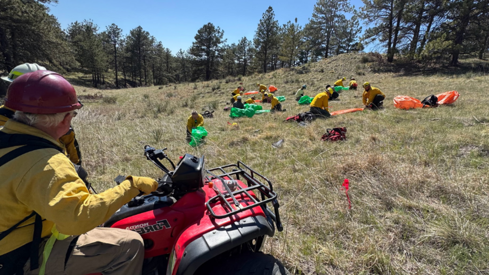 An instructor at Spring Wildland Fire Academy oversees fire students practicing a fire shelter deployment